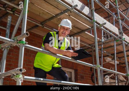 Male builder foreman, construction worker, contractor or architect on building site writing on black clipboard Stock Photo