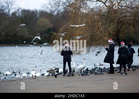People wearing Santa Claus hats feed birds in Hyde Park on Christmas Day in London. Stock Photo