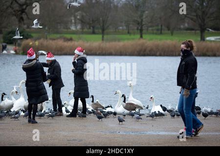 People wearing Santa Claus hats feed birds as pedestrians wearing face coverings walk past them in Hyde Park on Christmas Day in London.