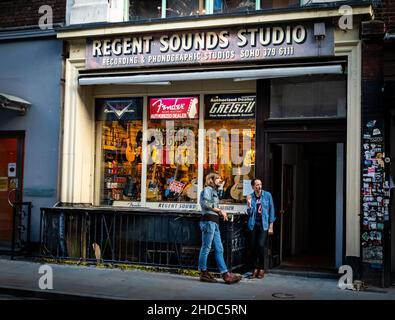 Two denim-clad rockers stand outside the famous music shop and recording studio Regent Sounds in Denmark St, London UK. Stock Photo