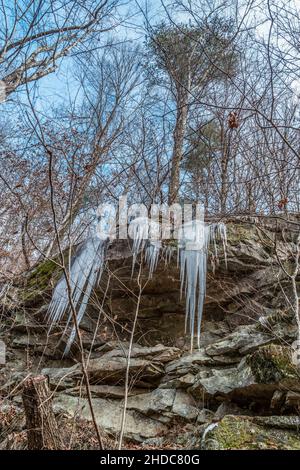 Looking upwards at the large icicles hanging from the cliff side of the rock formation in the mountains along the trail on a cold day in wintertime Stock Photo