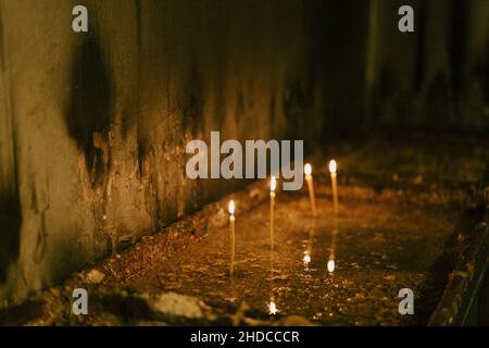 Candles are burning on a stand in front of a wall in a church Stock Photo