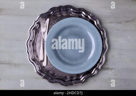 A blue plate with cutlery on a shiny metal tray on a light wooden table Stock Photo