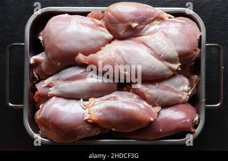 Photography of raw, skinless boneless chicken thighs in a metal bin on slate background for food illustration Stock Photo