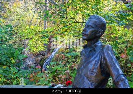 Miskolc, Hungary – October 26, 2019: Waterfall in beautiful autumn castle park of Lillafured. Blurred monument to famous Hungarian poet Jozsef Attila Stock Photo