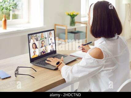 Adult woman sitting in front of laptop computer, attending webinar and taking notes Stock Photo
