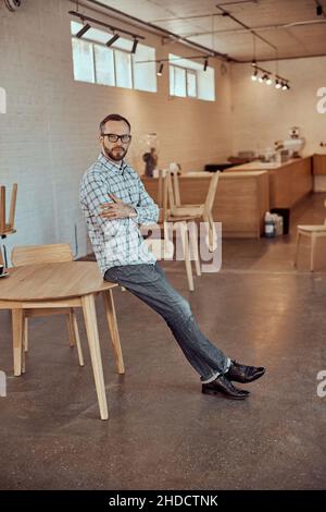 Bearded man sitting on the edge of table in cafe Stock Photo
