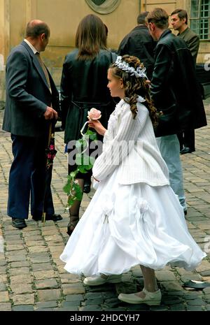 Lviv, Ukraine: A girl with long hair in a white dress and holding a pink rose. She is outside the Dominican Church or Church of the Holy Eucharist Stock Photo