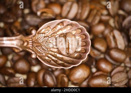 Top down view on isolated on vintage bronze spoon with one single isolated coffee bean, blurred beans background Stock Photo
