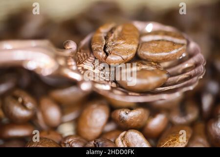 Macro closeup of vintage bronze spoon with three roasted coffee beans, blurred background Stock Photo