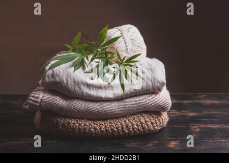 A stack of various types of hemp fiber fabrics. Hemp threads, yarn and fabric with cannabis leaves on a wooden background. Stock Photo
