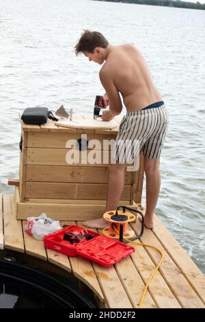 Man using a drill to add a corner brace to a cover on a boat under construction. Clitherall Minnesota MN USA Stock Photo