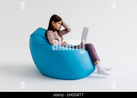 Child using laptop while resting on bean bag chair on white background Stock Photo