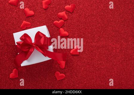White gift boxes with red ribbon and small red decorative hearts on red background. Top view with copy space. Valentines day or Wedding romantic conce Stock Photo