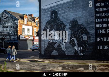 Two young woman walking past a Loyalist paramilitary mural on the Newtownards road on the 8th  November 2021 in Belfast,Northern Irland . Stock Photo