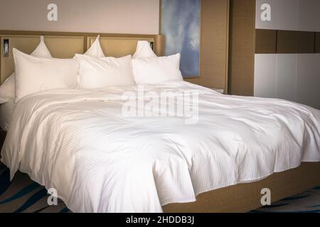 King sizes bed  with brown interior and white bright clean sheets and six pillows comfort. Luxurious stays and comfort concept. Stock Photo