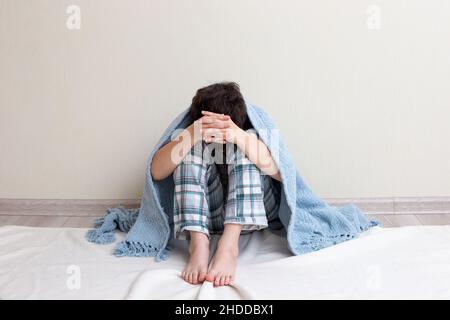 Teen boy sad, sitting in pajamas on the floor Stock Photo