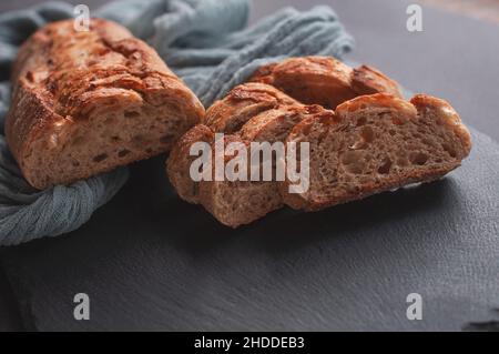 Sliced bread on a wooden table with a gray gauze tablecloth, fresh baguette on a wooden background Stock Photo