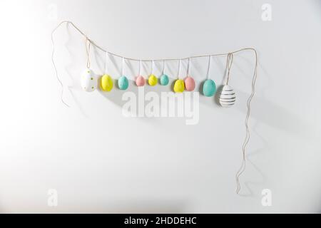 A garland of multi-colored plastic eggs hanging on a white wall. Home decoration for Easter Stock Photo