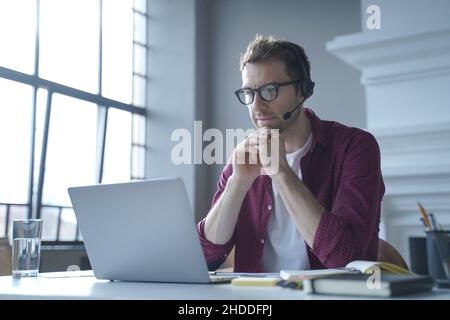 Pensive German businessman in headphones sits at desk while remotely working from home Stock Photo