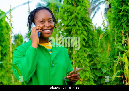 overexcited pretty african woman in the farm making calls in the farm while holding money on her other hand Stock Photo