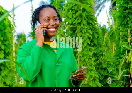 pretty african woman in the farm making calls in the farm while holding money on her other hand Stock Photo