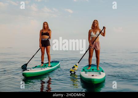June 25, 2021. Anapa, Russia. Slim girls rowing on stand up paddle board at quiet sea. Woman on Red Paddle SUP board in sea. Stock Photo