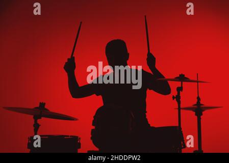 Silhouette of a young man playing drums on a red background. Stock Photo