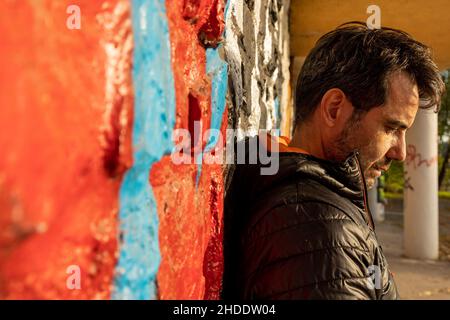 Closeup of a Caucasian man leaning against a stone wall covered in colorful graffiti Stock Photo