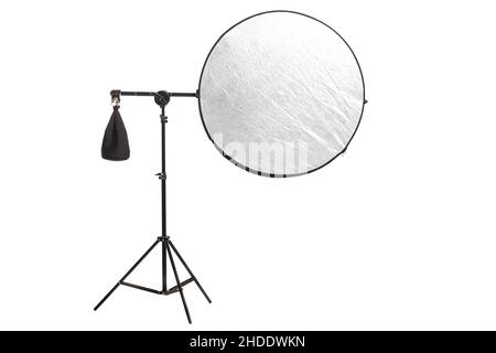 Round silver fabric reflector on stand with counterweight bag. Photography studio equipment isolated on white background. Stock Photo