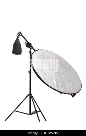 Round silver fabric reflector on stand with counterweight bag. Photography studio equipment isolated on white background. Stock Photo