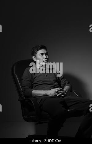 The modern man sitting on a chair and modern style in the studio, black and white Stock Photo