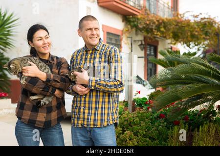 Smiling couple standing with cats near home Stock Photo