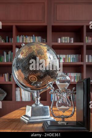 Chiang Rai,Thailand - Sep 06, 2020 : Hourglass and world desk globe on wooden table in library, Learning and education concepts. Selective focus. Stock Photo