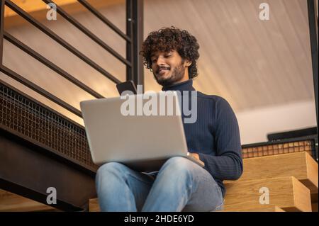 Man with laptop looking at smartphone sitting on stairs Stock Photo