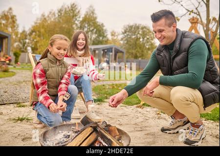 Man woman and girl crouched near fire with marshmallows Stock Photo
