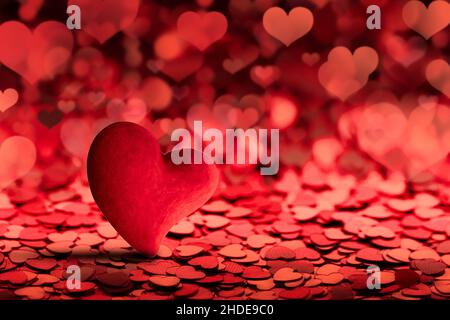 a beautiful red heart on a blurry dark red background of confetti and hearts. a concept for a matchmaking holiday party or a valentine card for congra Stock Photo