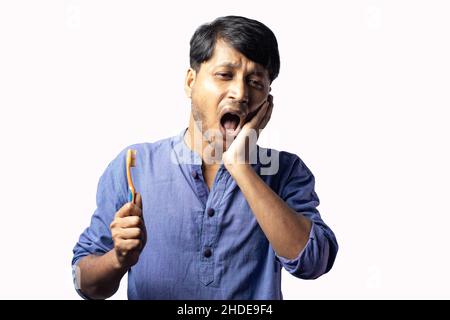 A young Indian male in blue dress facing teeth problem while brushing on white background Stock Photo