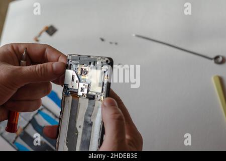A man is repairing a Smartphone. Hands hold a screwdriver and disconnect the sim card loop. Services Repair. Selective focus. Stock Photo