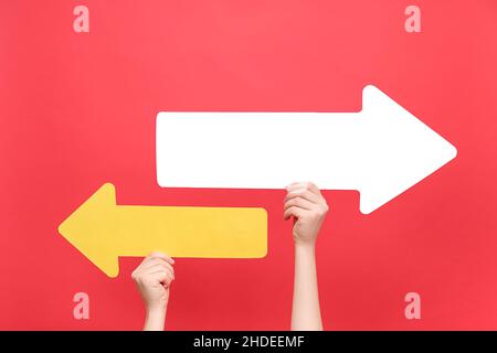 Close up of female hands holding two paper arrow pointing left and right, isolated on red color background studio with copy space for your text or des Stock Photo