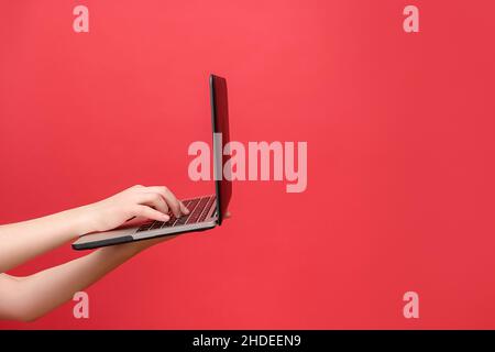 Close up of female hand holding working on laptop pc computer typing on keyboard, isolated over red studio background wall with copy space commercial Stock Photo