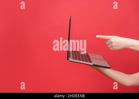 Cropped image of female hands holding and pointing on laptop, isolated over pastel red color background studio with copy space. Advertising workspace Stock Photo