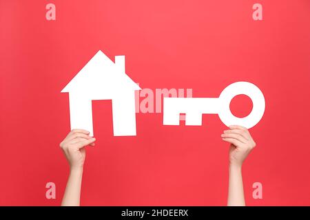 Close-up of female hands holding white paper keys and house model, isolated on pastel red background studio with copy space. Real estate, insurance co Stock Photo