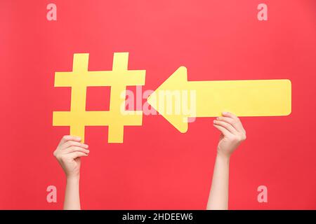 Close up of female hands holding big yellow hashtag and arrow, blogging blog website strategy, isolated on red color background wall in studio with co Stock Photo