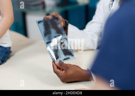 Closeup of african american pediatrician doctor holding lung radiography in hand discussing medical expertise during examination in hospital office. Therapist man analyzing xray. Medicine service Stock Photo