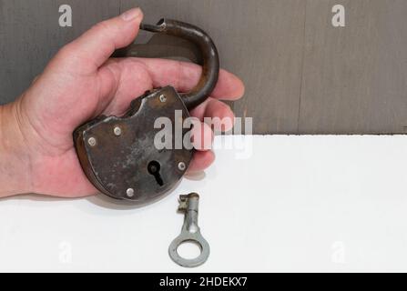 Old rusty padlock with key in hand close-up on white table Stock Photo