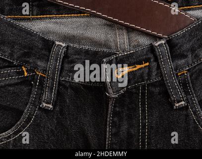 Black denim trousers with white strong stitching and leather belt close-up. Front view Stock Photo