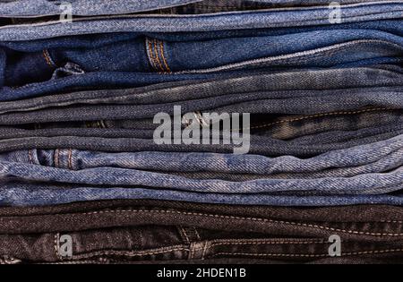 Stack of stock denim trousers of various models and colors close-up. Side view Stock Photo