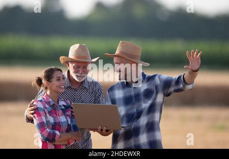 Group of happy farmers cooperating while working on a computer at agricultural field. Stock Photo