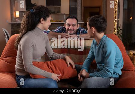Happy family of three, mother father and son sitting on sofa, talking and smiling Stock Photo